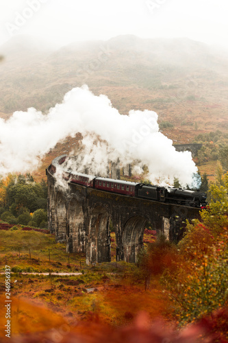 Steam train passing Glenfinnan Viaduct with fog covered mountains in the background during a moody autumn day (Glenfinnan, Scotland, Europe)