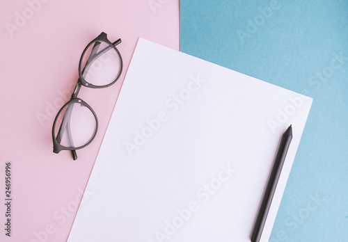 Office desk workspace with paper blank, pen and glasses on pink background.