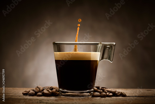 Black coffee in glass cup with coffee beans and jumping drop, on wooden table © winston