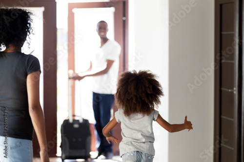 Fotografi Happy child daughter running to meet african dad coming home with suitcase, rear