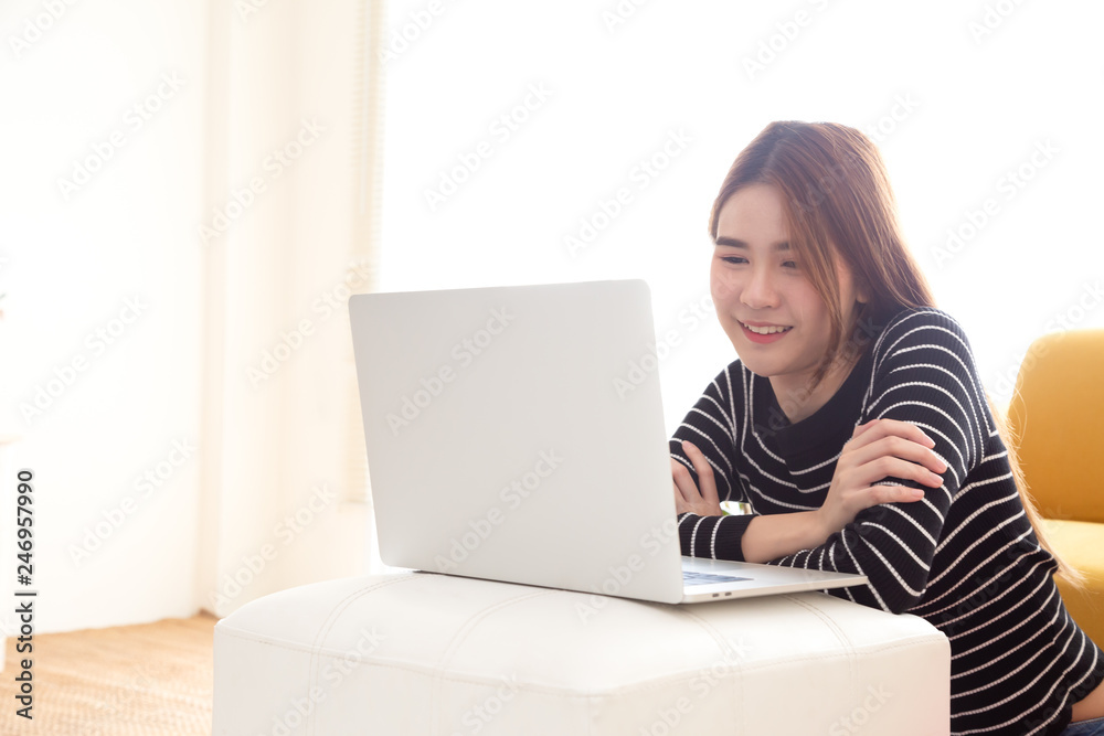 Naklejka premium Young Asian woman sitting on floor and watch movies, TV online with laptop computer in living room at home