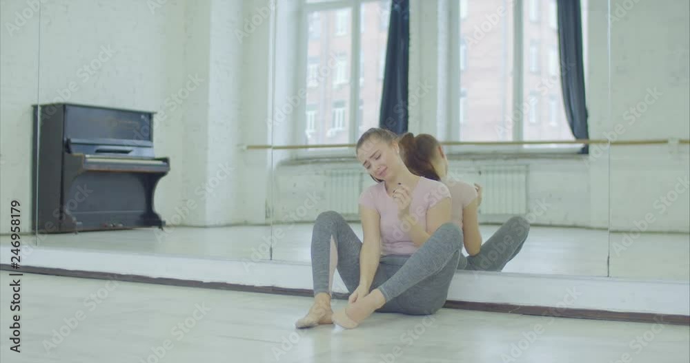 Desperate female dancer in tears taking off and throwing away ballet shoes in dance studio while sitting on the floor and leaning on big mirror. Upset crying woman disappointed with her performance. Desperate female dancer in tears taking off and throwing away ballet shoes in dance studio while sitting on the floor and leaning on big mirror. Upset crying woman disappointed with her performance.