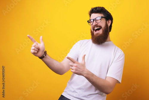 Indoor shot of cheerful bearded man in casual clothes indicates happily at handsome, has positive expression photo