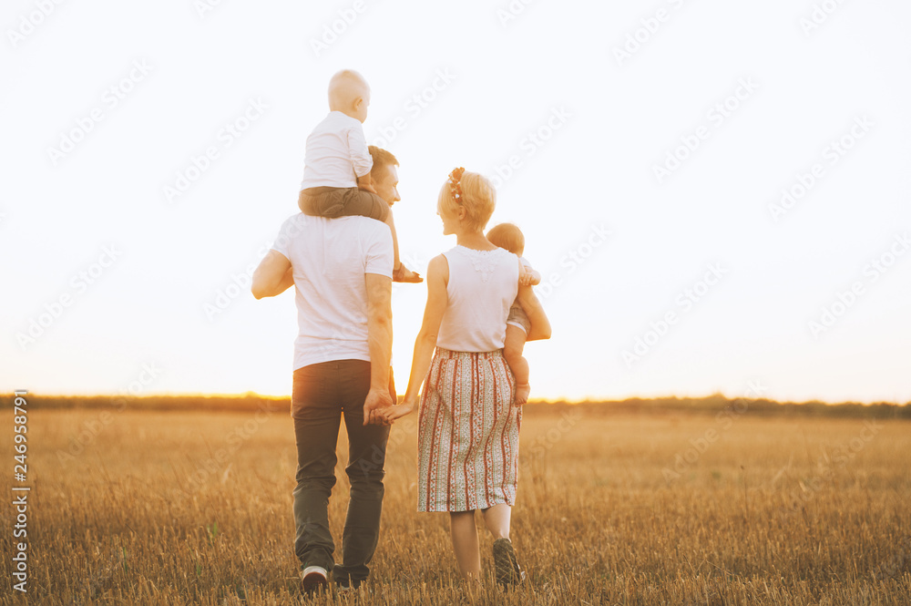 Fototapeta premium Happy young family is walking along the wheat field at sunset. The concept of family and love