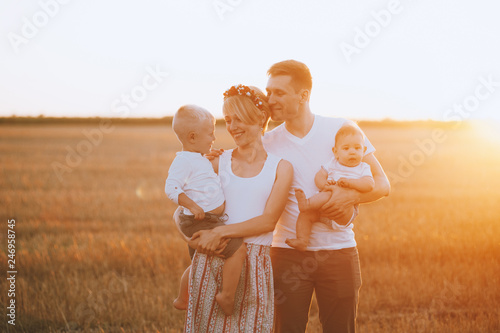 Happy young family holding their children on hands on nature in field on sunset