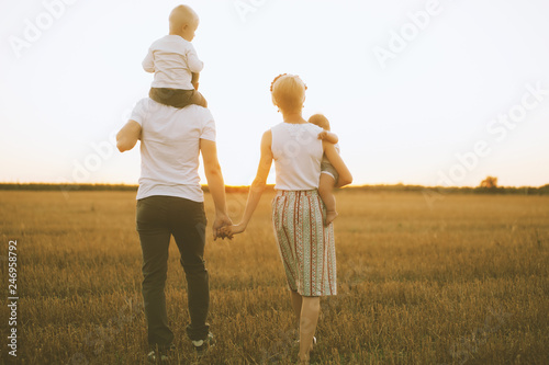 Happy ypung family father mom and two sons walking in a wheat field and watching the sunset