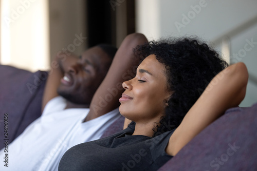 Relaxed african couple enjoying peaceful rest breathing fresh air at home on comfortable couch, happy lazy young black couple having nap leaning on sofa relaxing in living room feel no stress free