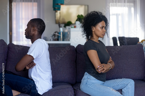 Stubborn black african couple sitting on couch turned back ignoring each other after fight quarrel, offended upset man and woman avoiding talk, family misunderstandings, selfishness in relationships photo