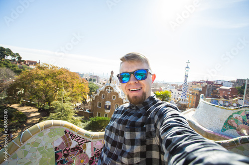 Photography Travel and holidays concept - Handsome man looking at camera taking photo with smart phone smiling in Park Guell, Barcelona, Spain
