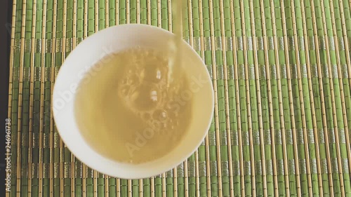 Green tea is poured into a small bowl that stands on a light mat. Top view.