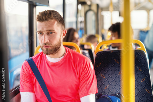 Young blonde sporty man with serious face sitting in the city bus.