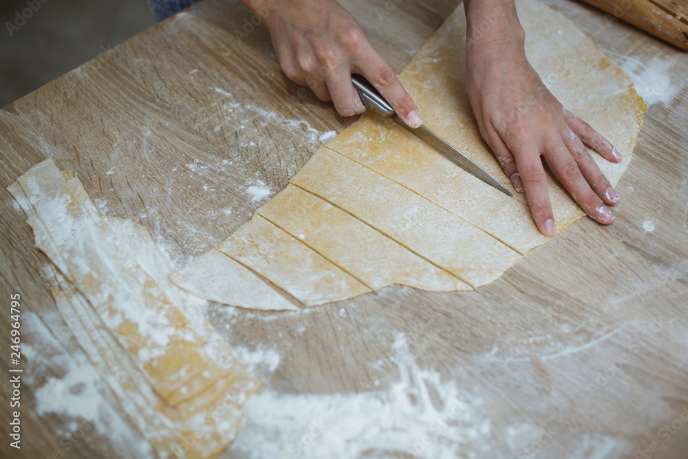 On the table lies the dough for noodles and the tools needed for cutting. The girl cuts small pieces. On the table lies the dough for noodles and the tools needed for cutting. The girl cuts small pieces.