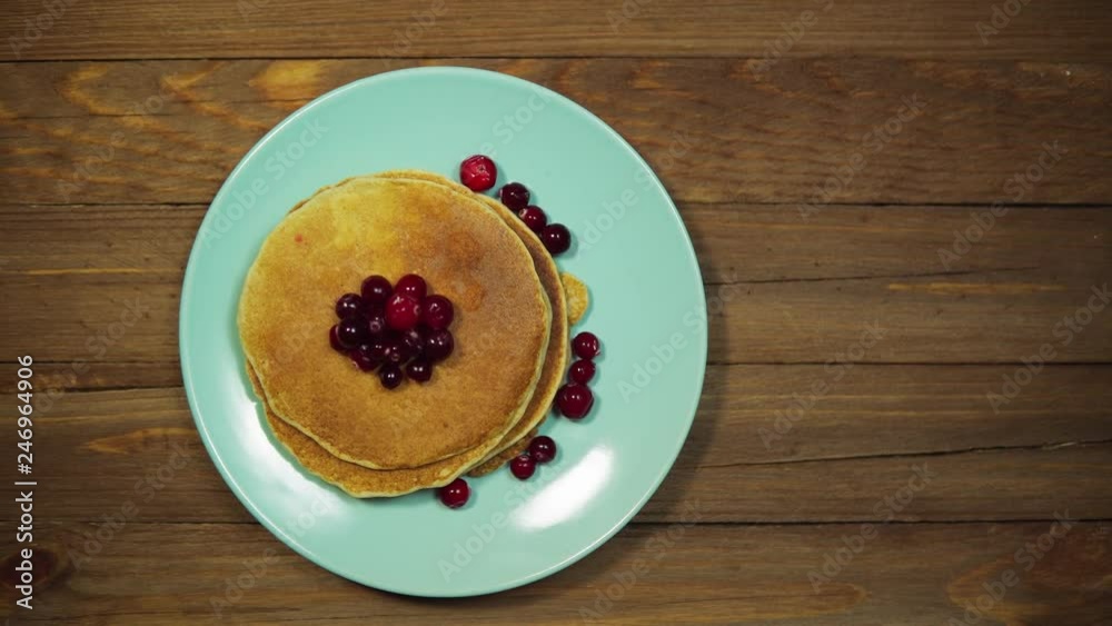 Top view someone serves a wooden table, hands put a fork and a knife on a blue plate with pancakes and red cranberries berries, the camera moves from right to left. Top view someone serves a wooden table, hands put a fork and a knife on a blue plate with pancakes and red cranberries berries, the camera moves from right to left.