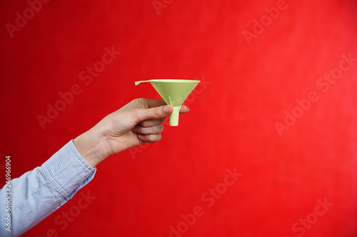 Female hand holding a green funnel on a red background. Sifting the truth. Be able to analyze.