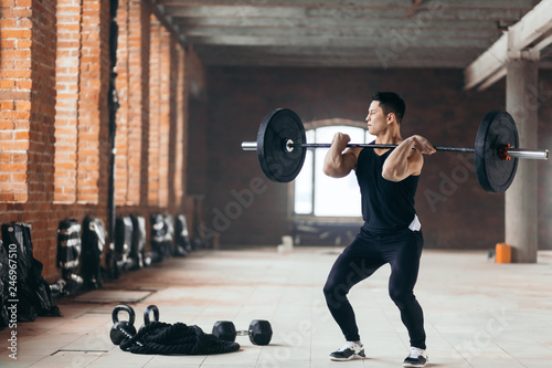 Handsome man doing squats with barbell in the sport center. guy is fond of professional sport. full length photo. copy space photo