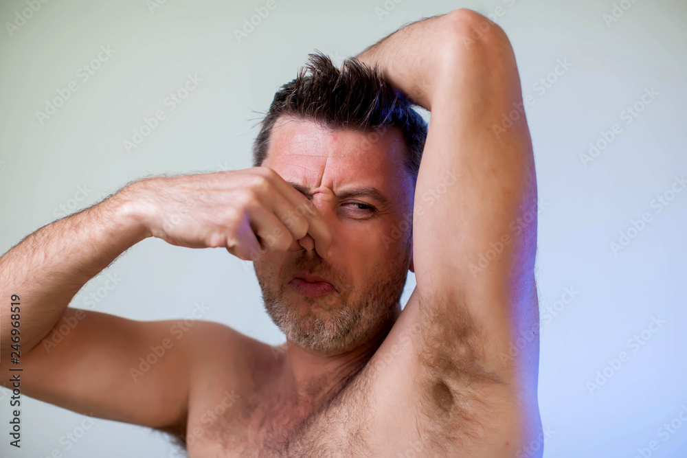 Close up portrait of man, smelling his armpit, feeling bad odor, wants to take a shower, needs antiperspirants Close up portrait of man, smelling his armpit, feeling bad odor, wants to take a shower, needs antiperspirants