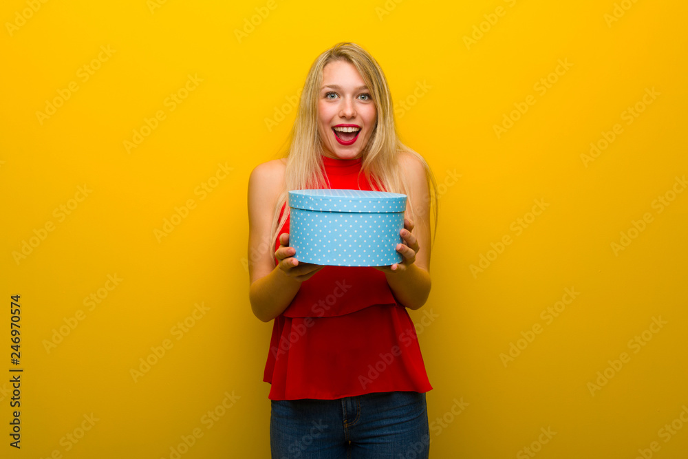Young girl with red dress over yellow wall surprised because has been given a gift Young girl with red dress over yellow wall surprised because has been given a gift