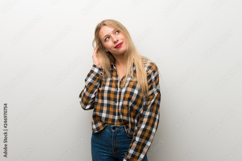 Blonde young girl over white wall thinking an idea while scratching head Blonde young girl over white wall thinking an idea while scratching head
