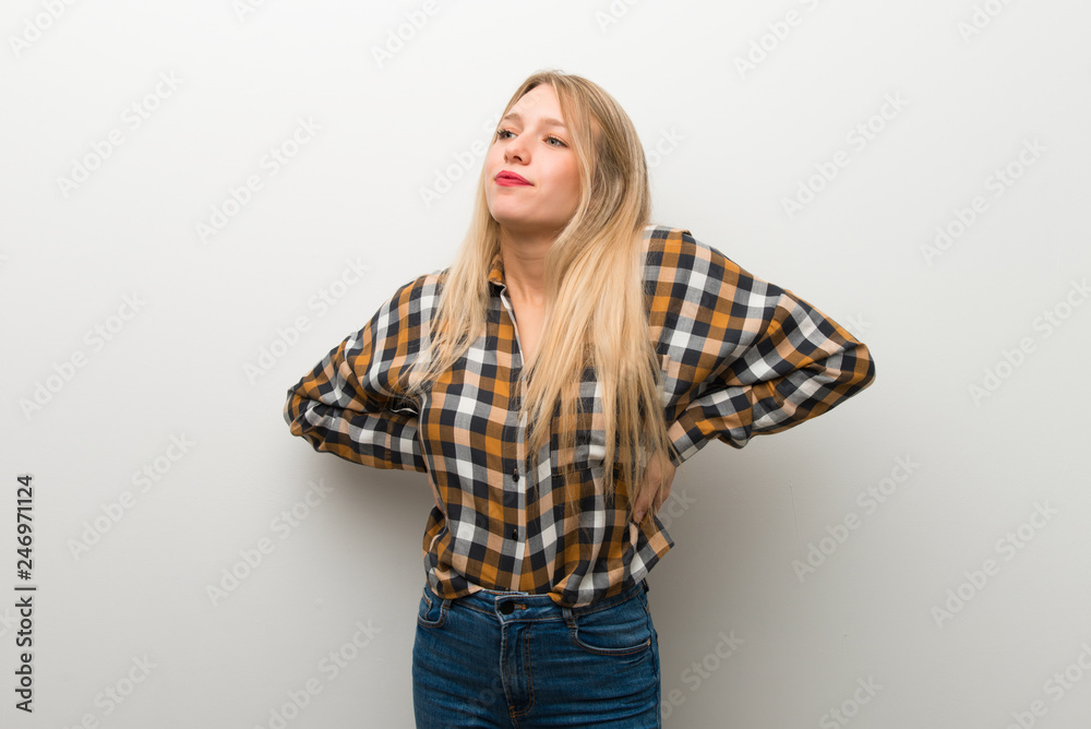 Blonde young girl over white wall suffering from backache for having made an effort Blonde young girl over white wall suffering from backache for having made an effort