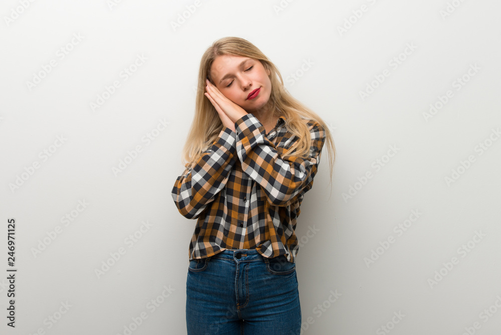 Blonde young girl over white wall making sleep gesture in dorable expression Blonde young girl over white wall making sleep gesture in dorable expression
