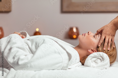 relaxed gorgeous girl with closed eyes lying in bathrobe and getting a facial massage in the clinic. close up side view photo