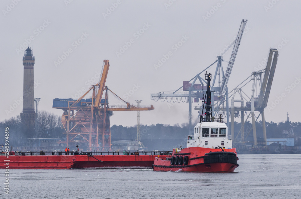 RED TUGBOAT, LIGHTHOUSE AND PORT CRANES  - A small ship departs from the port of Swinoujście by towing a barge