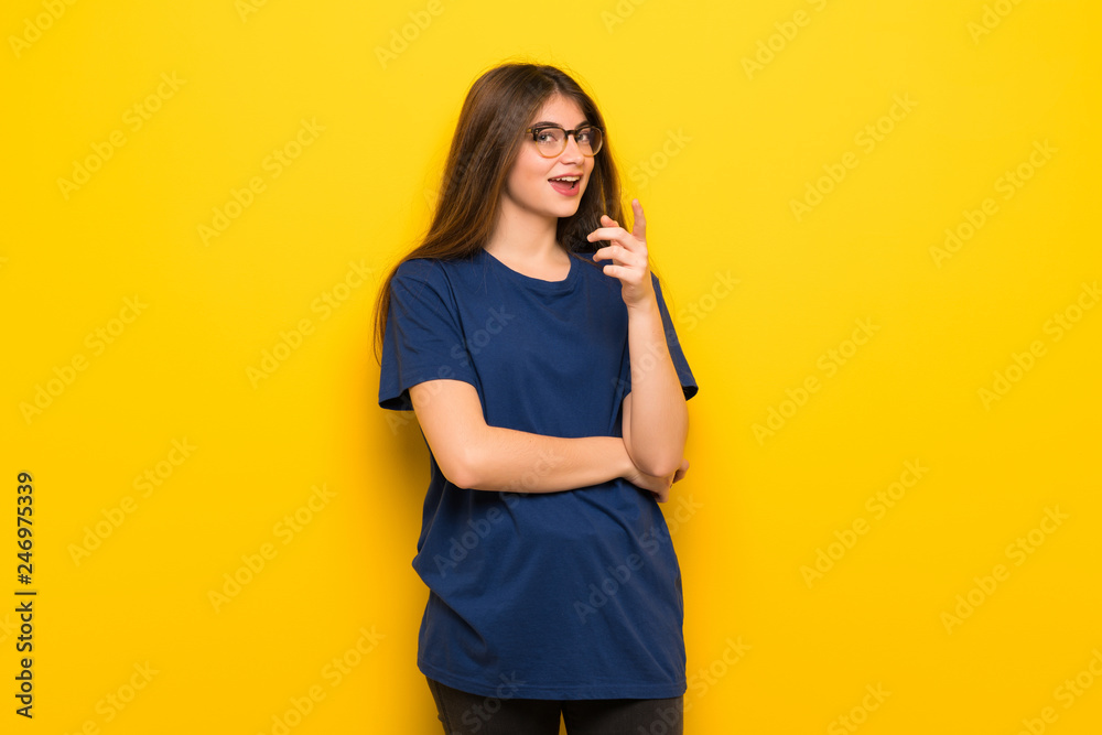 Young woman with glasses over yellow wall points finger at you with a confident expression Young woman with glasses over yellow wall points finger at you with a confident expression
