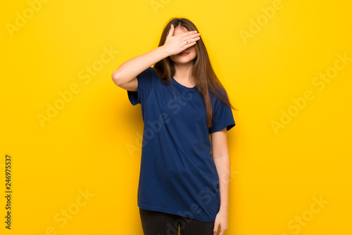 Young woman with glasses over yellow wall covering eyes by hands. Do not want to see something