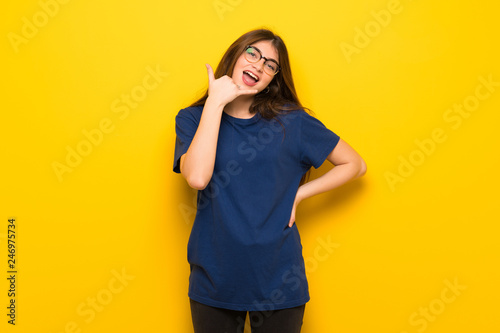 Young woman with glasses over yellow wall making phone gesture. Call me back sign © luismolinero