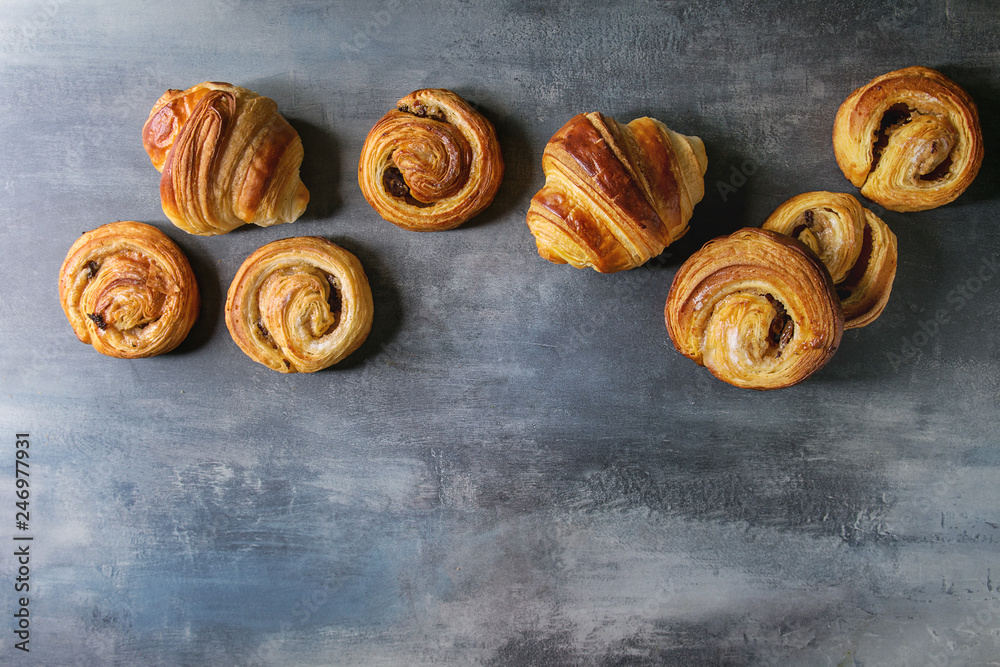 Fototapeta premium Variety of homemade puff pastry buns cinnamon rolls and croissant in row over blue texture background. Flat lay, space