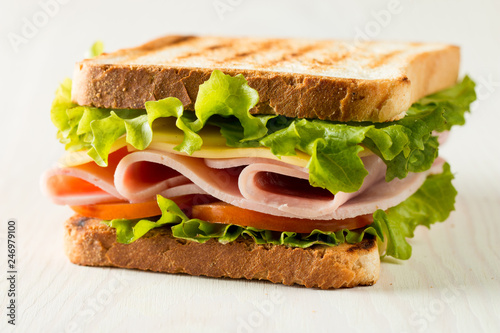 Close-up photo of a club sandwich. Sandwich with meat, prosciutto, salami, salad, vegetables, lettuce, tomato, onion and mustard on a fresh sliced rye bread on wooden background. Olives background.