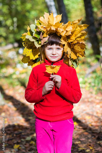 portrait of a girl in a red sweater with a wreath of autumn leaves on her head in the forest