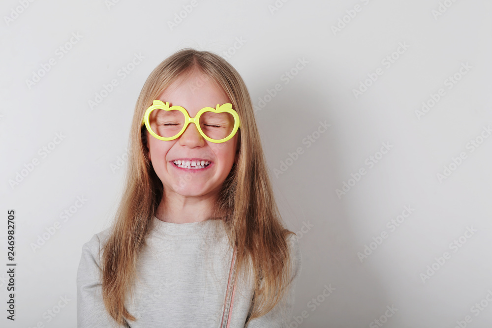 Portrait of happy laughing little girl in glasses making faces at camera. Expressive facial expressions . Human emotions, reactions, feelings and attitude . Portrait of happy laughing little girl in glasses making faces at camera. Expressive facial expressions . Human emotions, reactions, feelings and attitude .