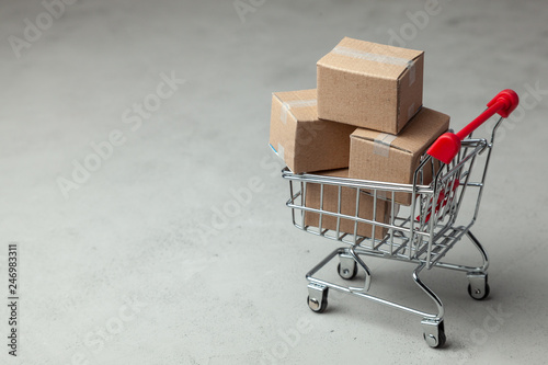 Buying goods in the online store. Cardboard boxes in the shopping basket on gray background.