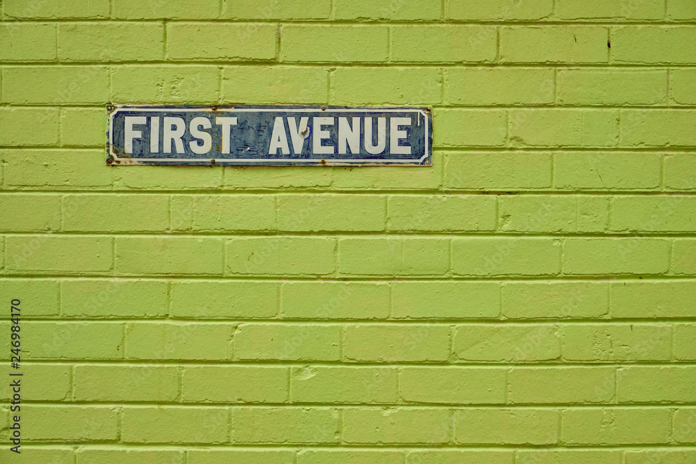 Obraz premium Vintage First Avenue street sign, on a green painted brick wall. Sign is old and shows major sign of wear and some rust