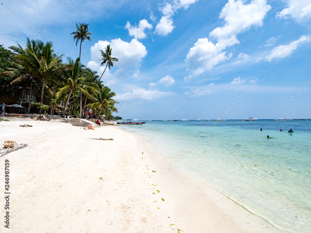 Beautiful tropical beach background from Alona Beach at Panglao Bohol island with beach chairs on the white sand beach with cloudy blue sky and palm trees. Travel Vacation, november 2018