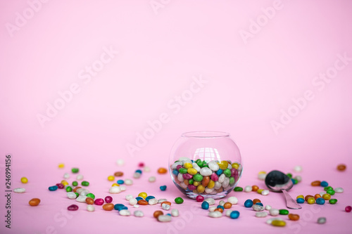 colorful candy in clear wrappers piled in a glass vase isolated on pink background
