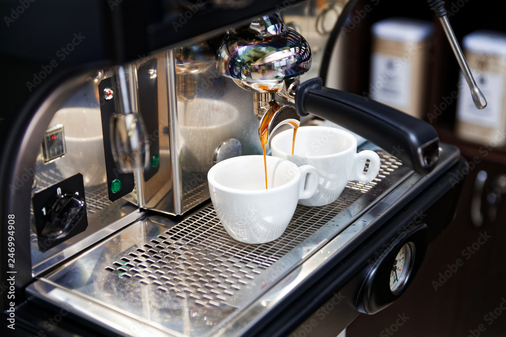 Coffee brewing in coffee machine. Espresso pouring in two white cups. Shallow focus, dark blurred background. Coffee brewing in coffee machine. Espresso pouring in two white cups. Shallow focus, dark blurred background.