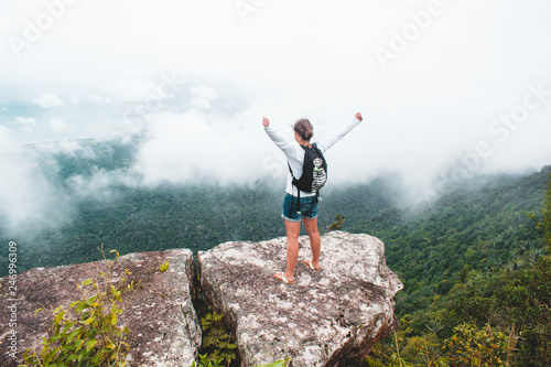 Caucasian female backpacker standing on a rock looking over a valley covered in clouds on Bokor Mountain in Cambodia