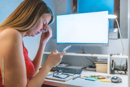 Sad woman talking on phone while making notes, sitting at her working place at home