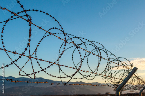 Barbed wire fence against the blue sky and mountains. Restraint, private property