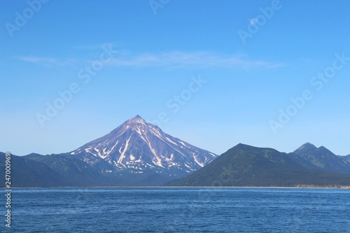 View of Vilyuchinsky volcano  also called Vilyuchik  from water. It s a stratovolcano in the southern part of Kamchatka Peninsula  Russia. Moon is visible in the sky.