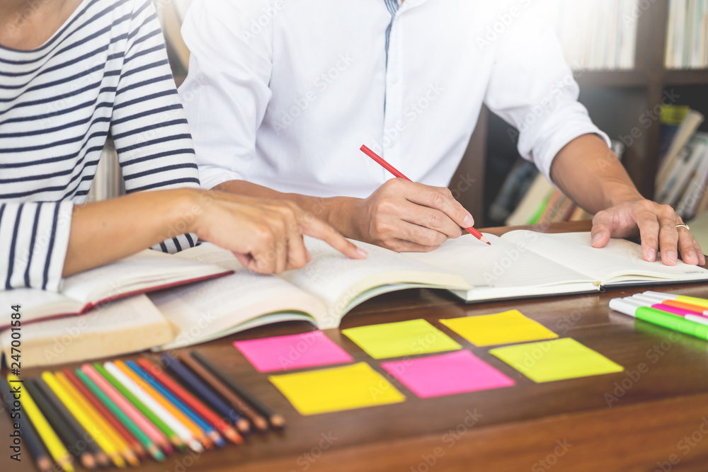 Young students classmates help friend catching up workbook and learning tutoring in a library, education and school concept Young students classmates help friend catching up workbook and learning tutoring in a library, education and school concept
