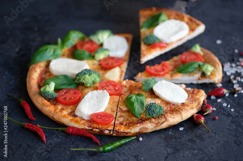 Sliced pizza with Mozzarella cheese, tomatoes, broccoli, Spices and fresh basil. Italian pizza. Pizza on black stone background