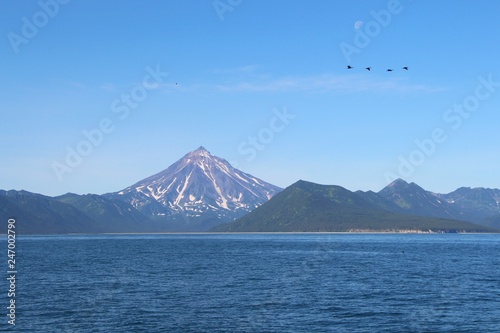View of Vilyuchinsky volcano  also called Vilyuchik  from water. It s a stratovolcano in the southern part of Kamchatka Peninsula  Russia. Moon is visible in the sky.