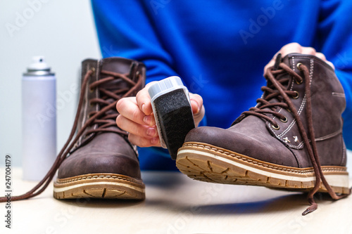 A person is cleaning men's suede casual boots with brush and spray. Shoe care. Footwear moisture and dirt protection photo