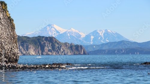 Rocky reef by Starichkov island near Kamchatka Peninsula, Russia. Avachinsky and Kozelsky volcanoes are visible in the background. photo