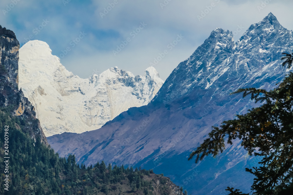 View on Manaslu from Annapurna Circuit Trek, Himalayas, Nepal.Snowy peak of the mountain in the back. Some branches of the tree on the left. Gorge separating mountains in three parts