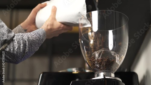 A close-up of an empty container on the top of the coffee machine and man's hands holding an open packet with coffee beans and start pouring beans into the container. Coffee making in a bar