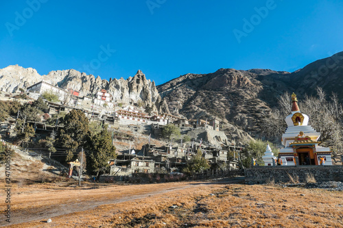 A temple complex in Manang Annapurna Circuit Trek, Nepal. Stupa in front of other buildings. Temple built on a rocky mountain hills. Sacred place for many Buddhist tourists. Dry land. Clear sky.